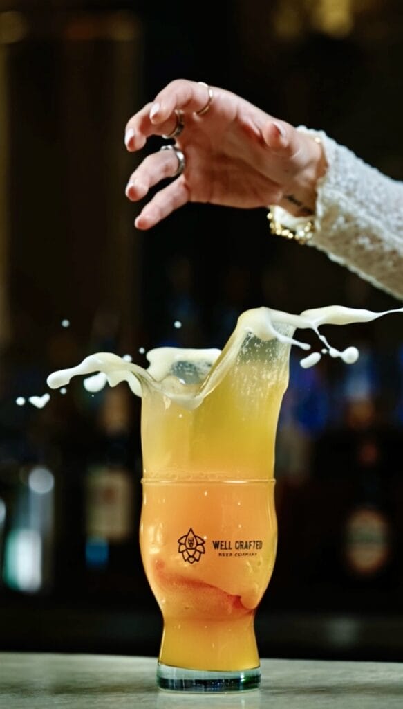 A pint glass of Well Crafted Beer splashing